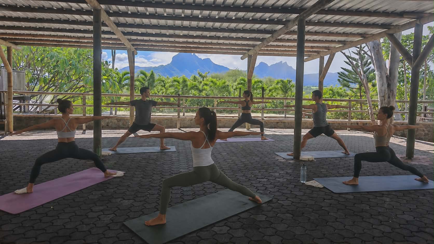 Yoga session on the Upper Deck at sunrise, framed by mountains and tropical foliage in Tamarin